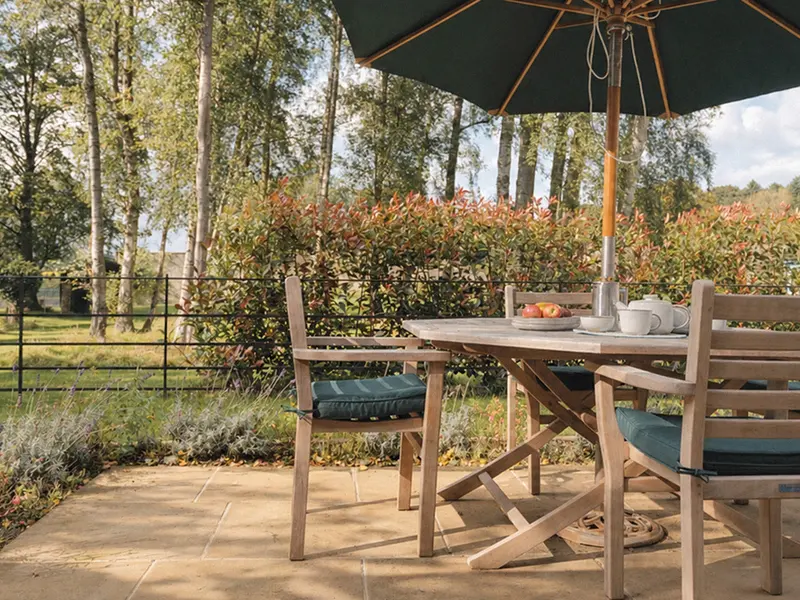 Outdoor dining table and chairs beneath a parasol beside the garden